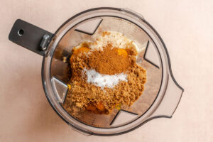 Overhead view of a blender containing brown sugar, cinnamon, salt, and other ingredients, ready to be mixed.