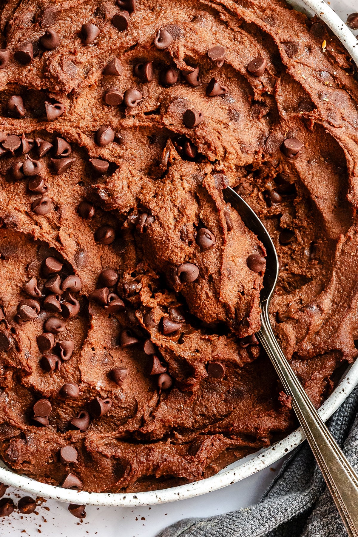 A bowl of brownie batter hummus being scooped with a metal spoon.