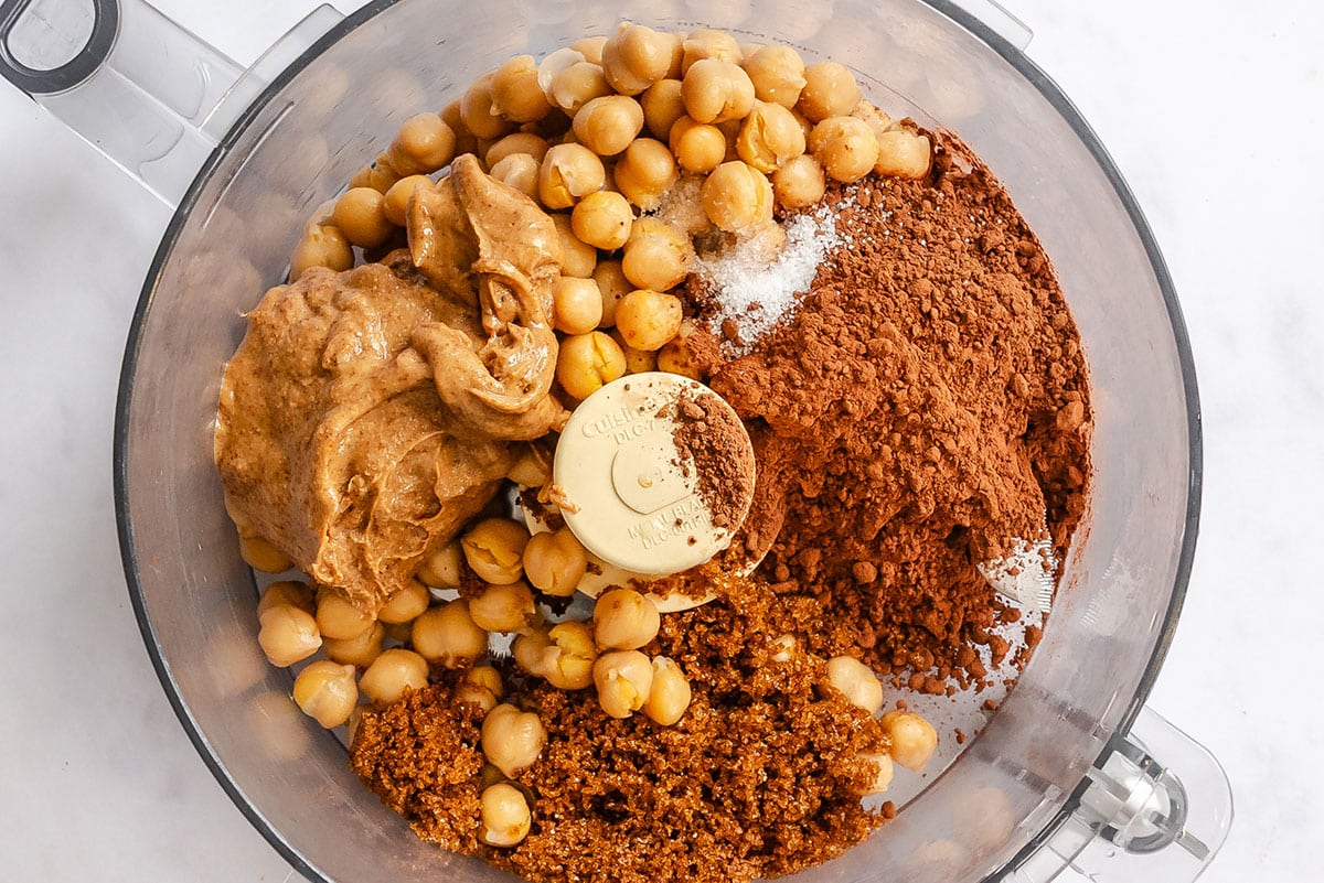 Chickpeas, peanut butter, cocoa powder, and brown sugar in a food processor bowl to make chocolate hummus.