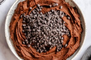 A white speckled bowl filled with brownie batter dessert hummus topped with a mound of chocolate chips.
