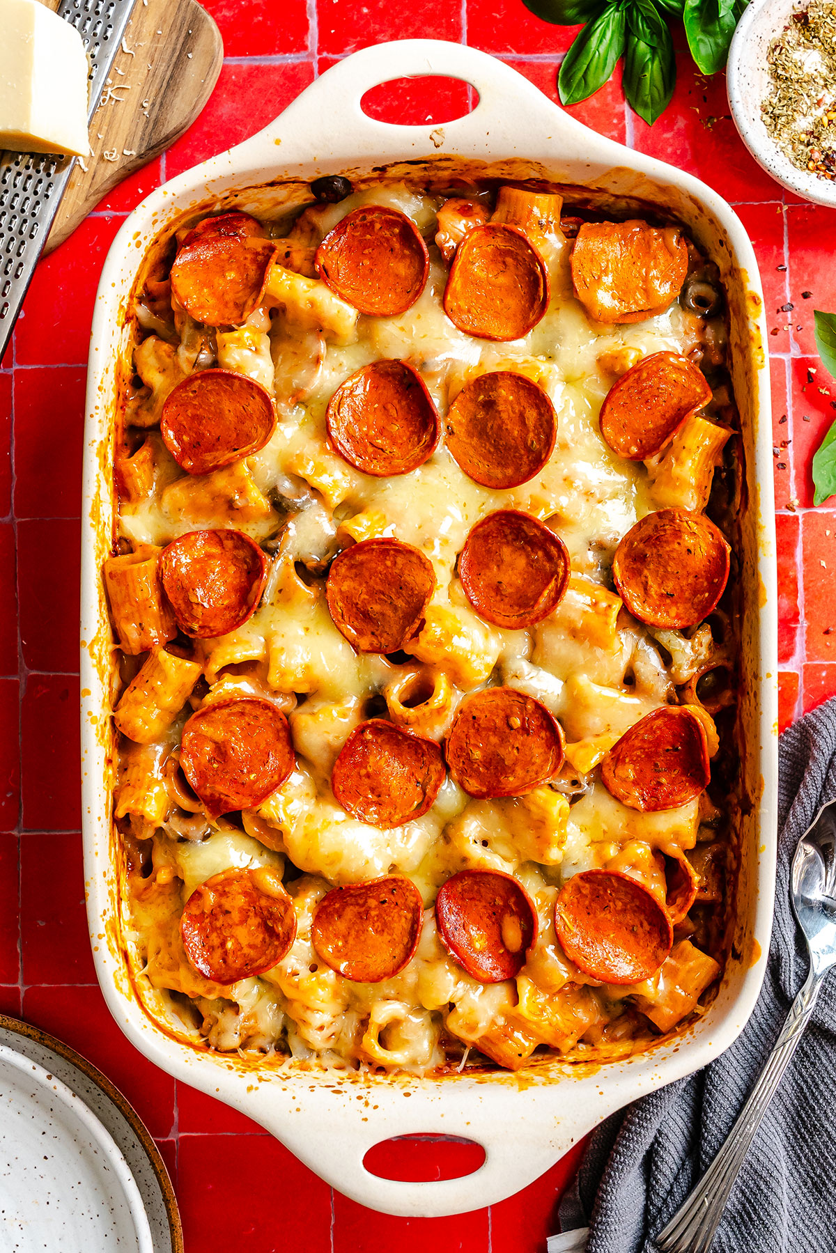 Baked rigatoni pasta with melted cheese and pepperoni slices in a white ceramic baking dish.