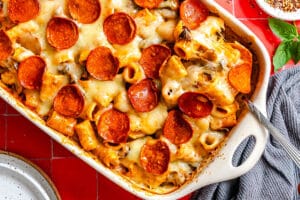 Baked ziti with melted cheese and pepperoni slices in a ceramic baking dish.