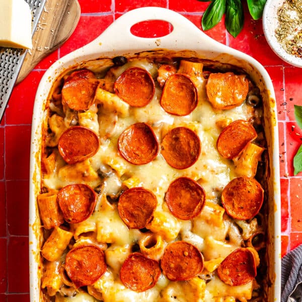 Baked rigatoni pizza pasta with melted cheese and pepperoni slices in a white ceramic baking dish.