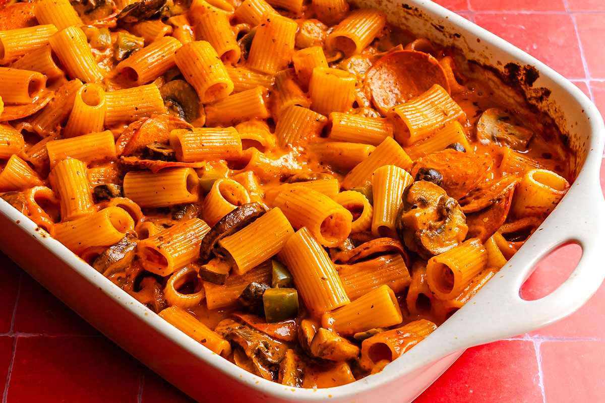 Baked rigatoni pasta with tomato sauce, pepperoni, and mushrooms in a white ceramic baking dish.