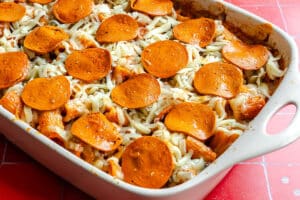 Baked pasta casserole topped with shredded cheese and pepperoni slices in a white baking dish.