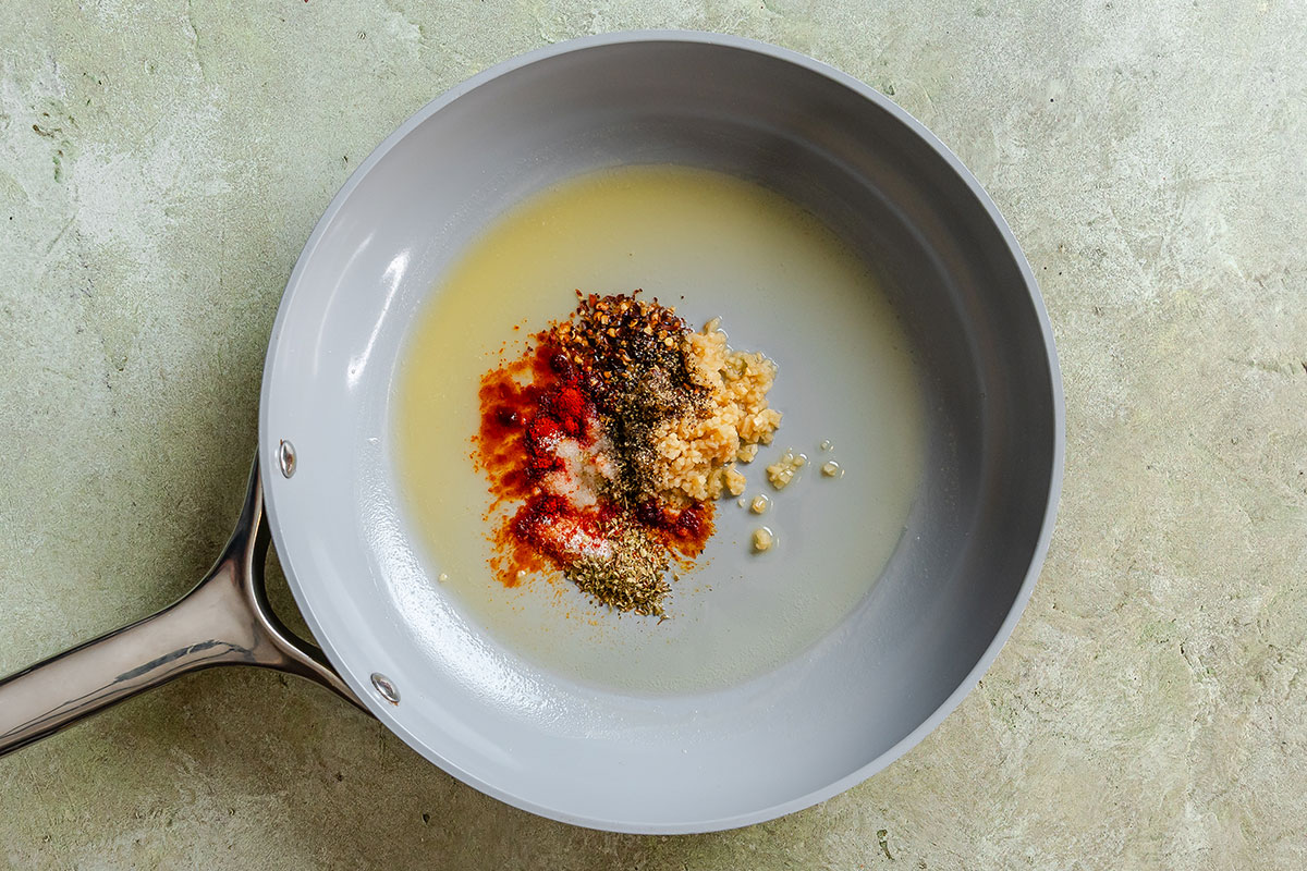 A frying pan containing melted butter, minced garlic, and a pile of mixed spices.