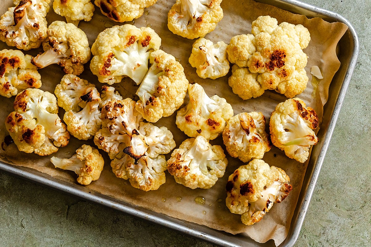 Roasted cauliflower florets on a parchment-lined baking sheet.