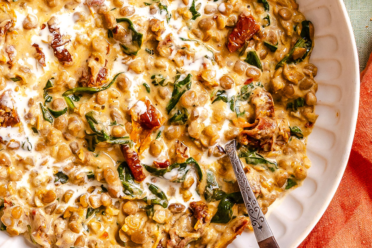 Creamy lentils with spinach and sun-dried tomatoes in a white bowl with a spoon.