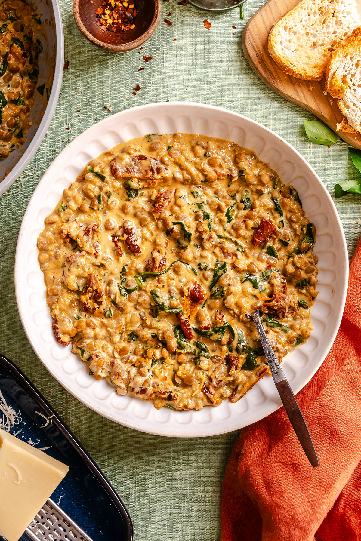 Creamy lentil stew with spinach and sun-dried tomatoes in a white bowl with a spoon.