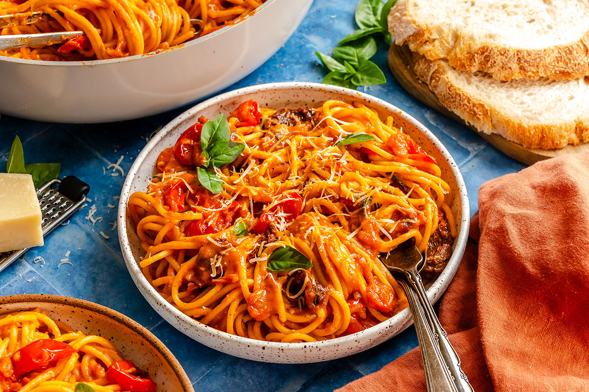 A bowl of creamy tomato pasta with cherry tomatoes and fresh basil, served with sliced bread.