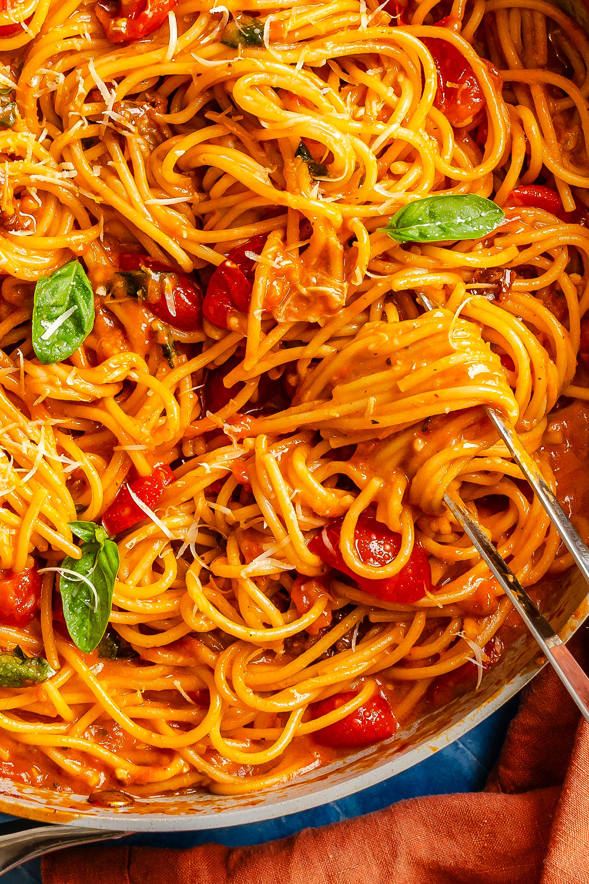 Spaghetti with tomato sauce, cherry tomatoes, and basil leaves in a pan, being lifted with a fork.