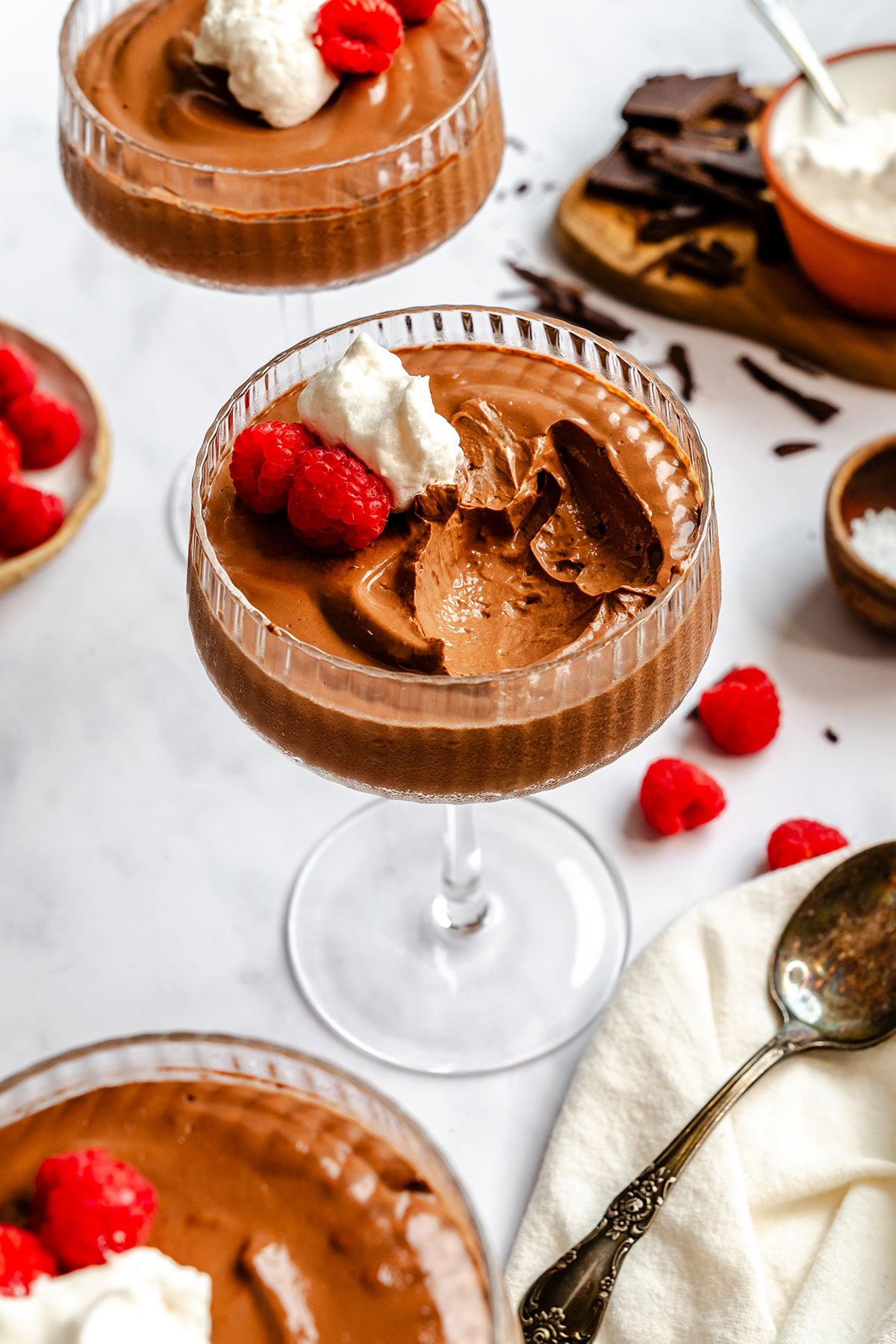 Chocolate mousse in a glass coupe, topped with whipped cream and raspberries.