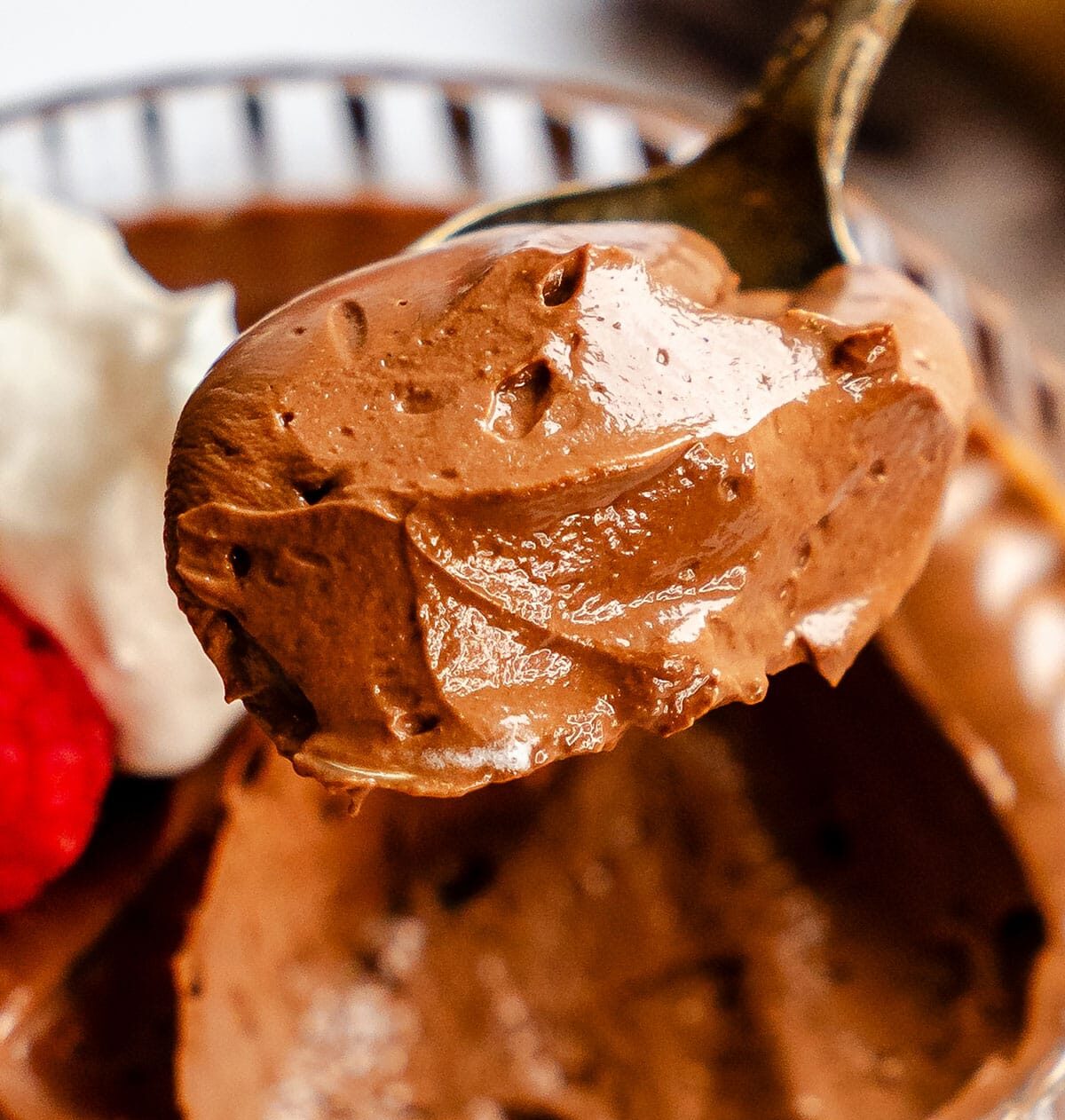A spoonful of chocolate mousse held above a glass dish with whipped cream and a strawberry.