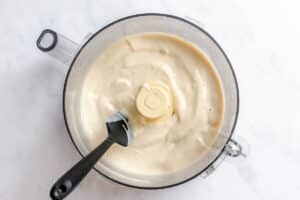 A food processor bowl containing creamy blended sauce and a black spatula.