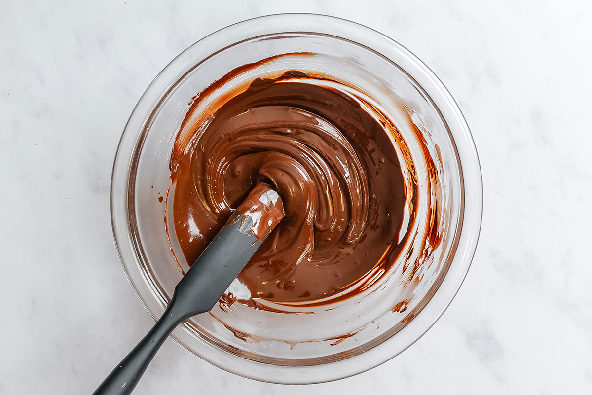 A glass bowl filled with melted chocolate being stirred by a silicone spatula.