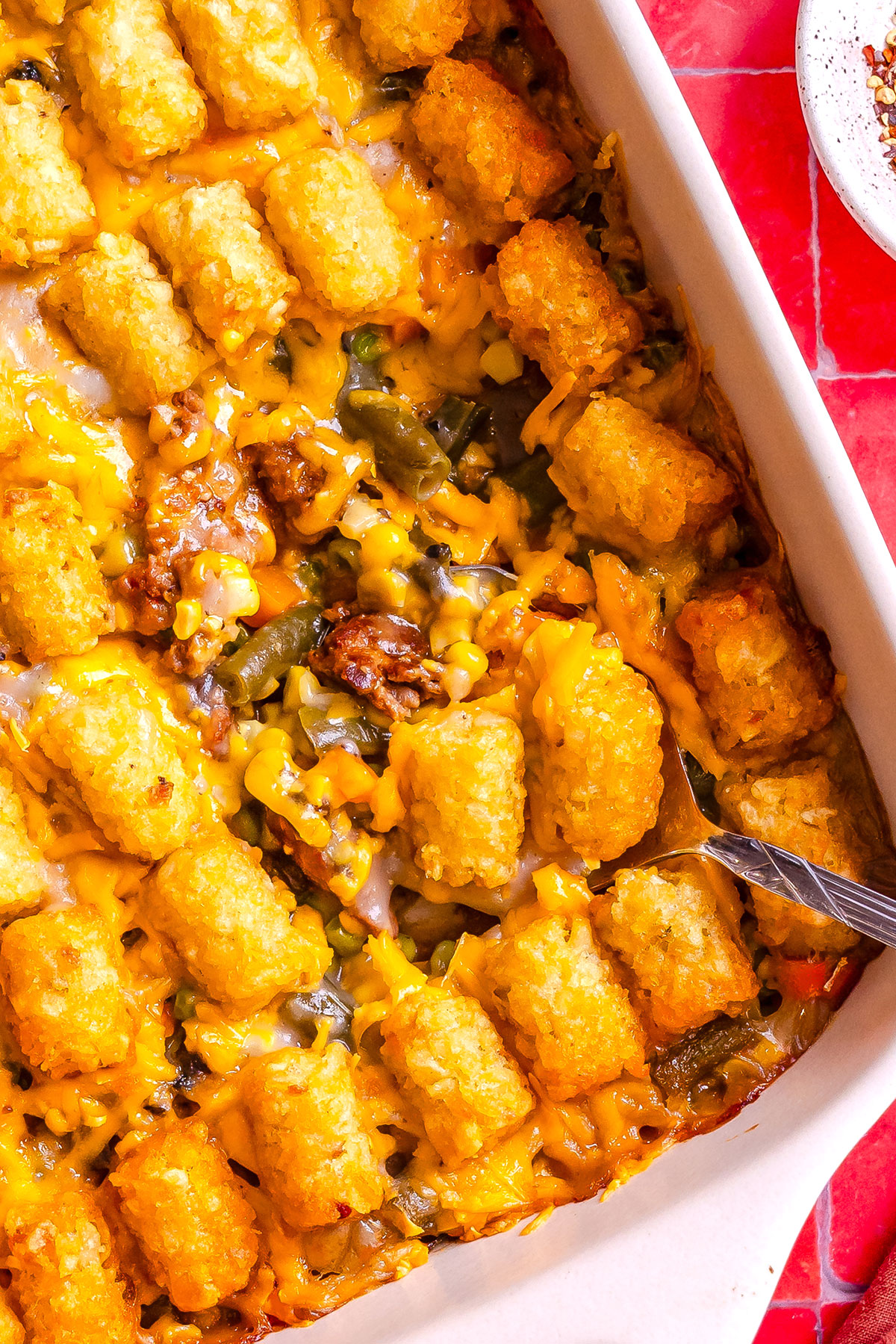 Tater tot casserole with melted cheese, green beans, and ground meat in a white baking dish.