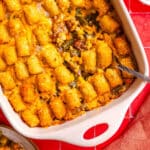 Tater tot casserole with melted cheese in a white baking dish with a serving spoon.