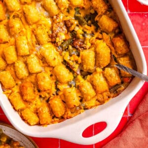 Tater tot casserole with melted cheese in a white baking dish with a serving spoon.