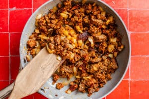 A wooden spatula stirring ground meat and chopped onions in a skillet.