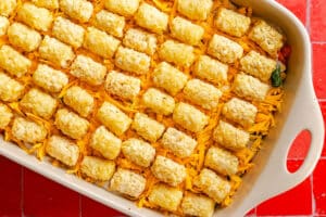 A baking dish filled with a casserole topped with shredded cheddar cheese and a grid of tater tots.