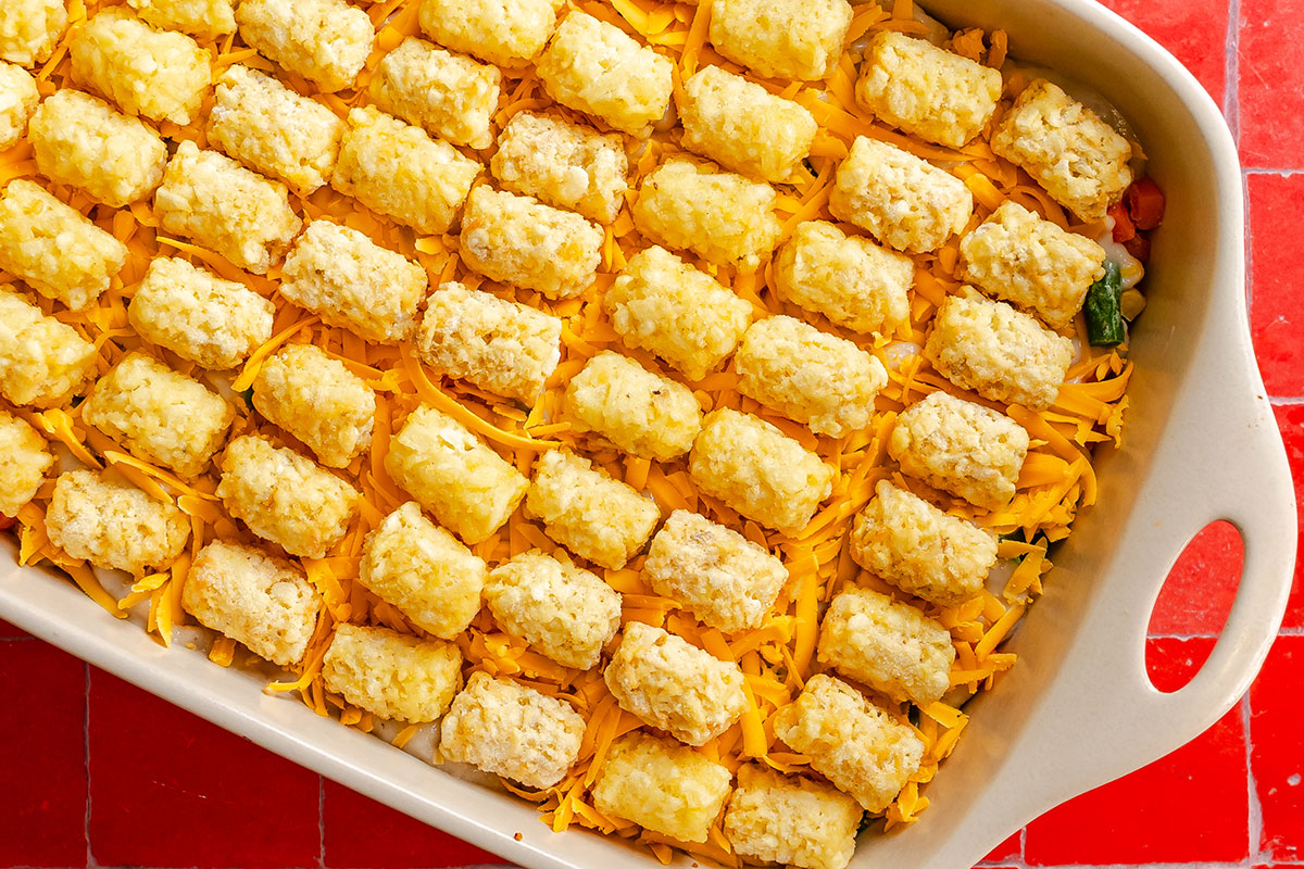 A baking dish filled with a casserole topped with shredded cheddar cheese and a grid of tater tots.